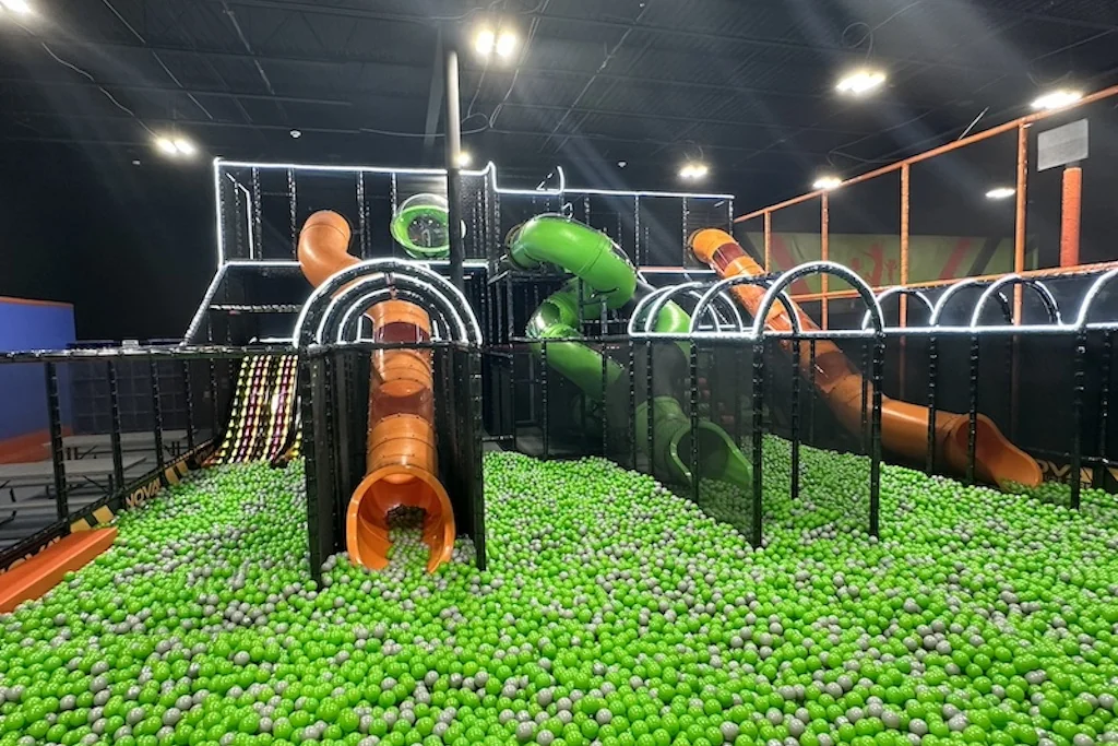 Piscina de pelotas verde con toboganes naranjas y verdes en Nova Adventure Park