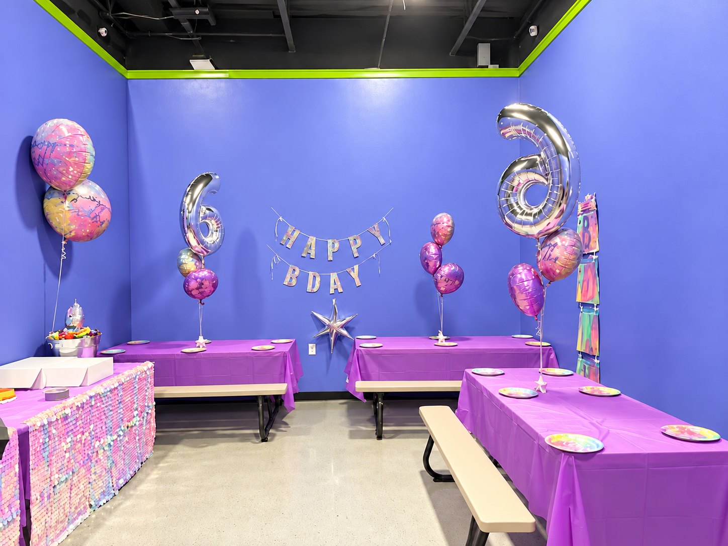 Salón de fiestas de Nova decorado con globos plateados de números, una pancarta de Happy Bday y mesas moradas